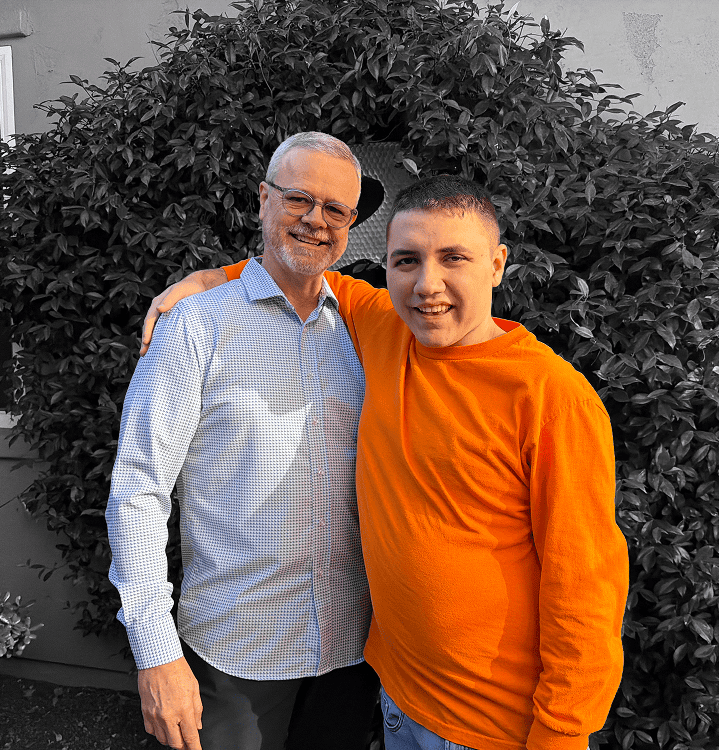 J Brad and Sam Britton smiling together, representing a journey of nonspeaking autism advocacy and connection.